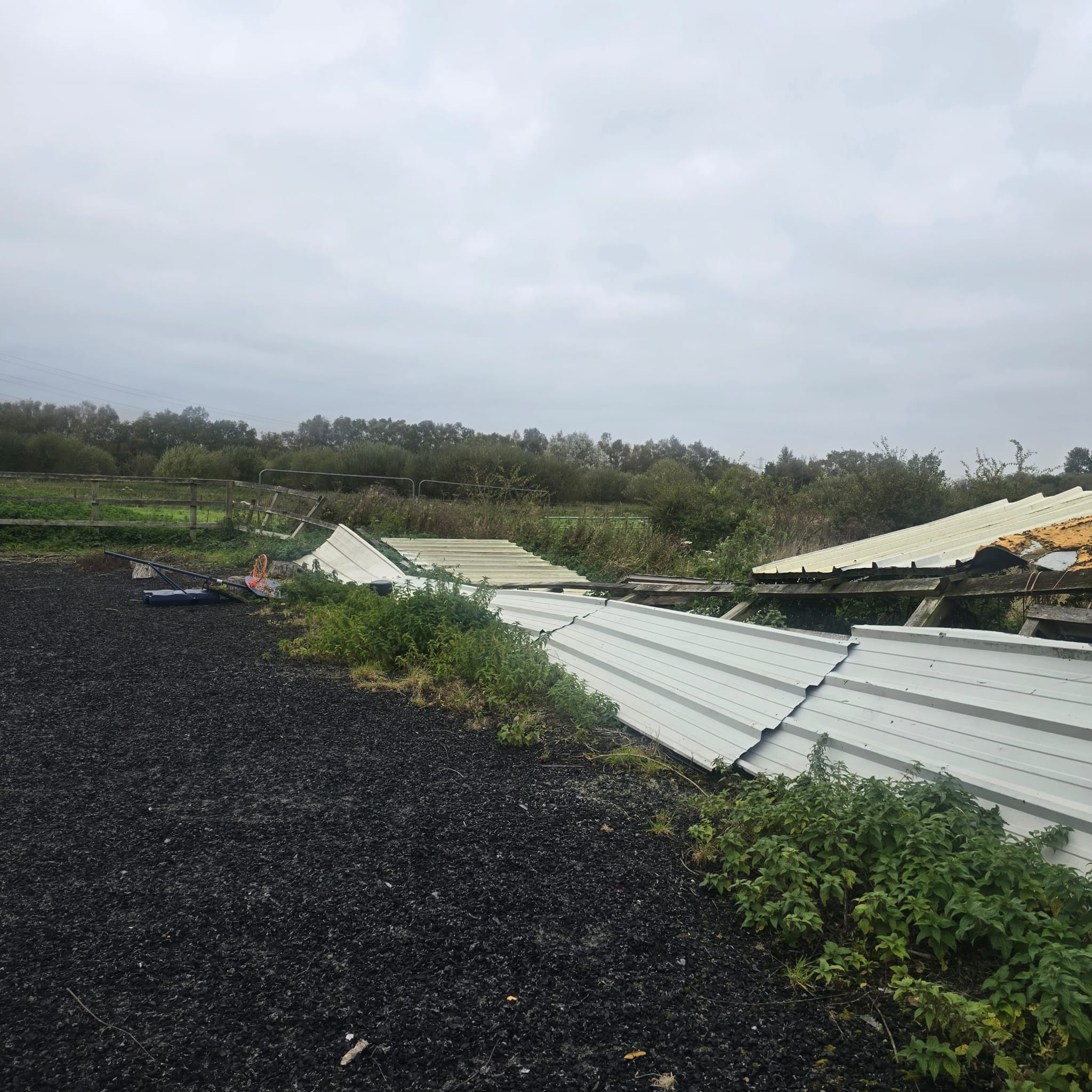 Corrugated roof sheets lying flat across the edge of the arena beside the fallen fence