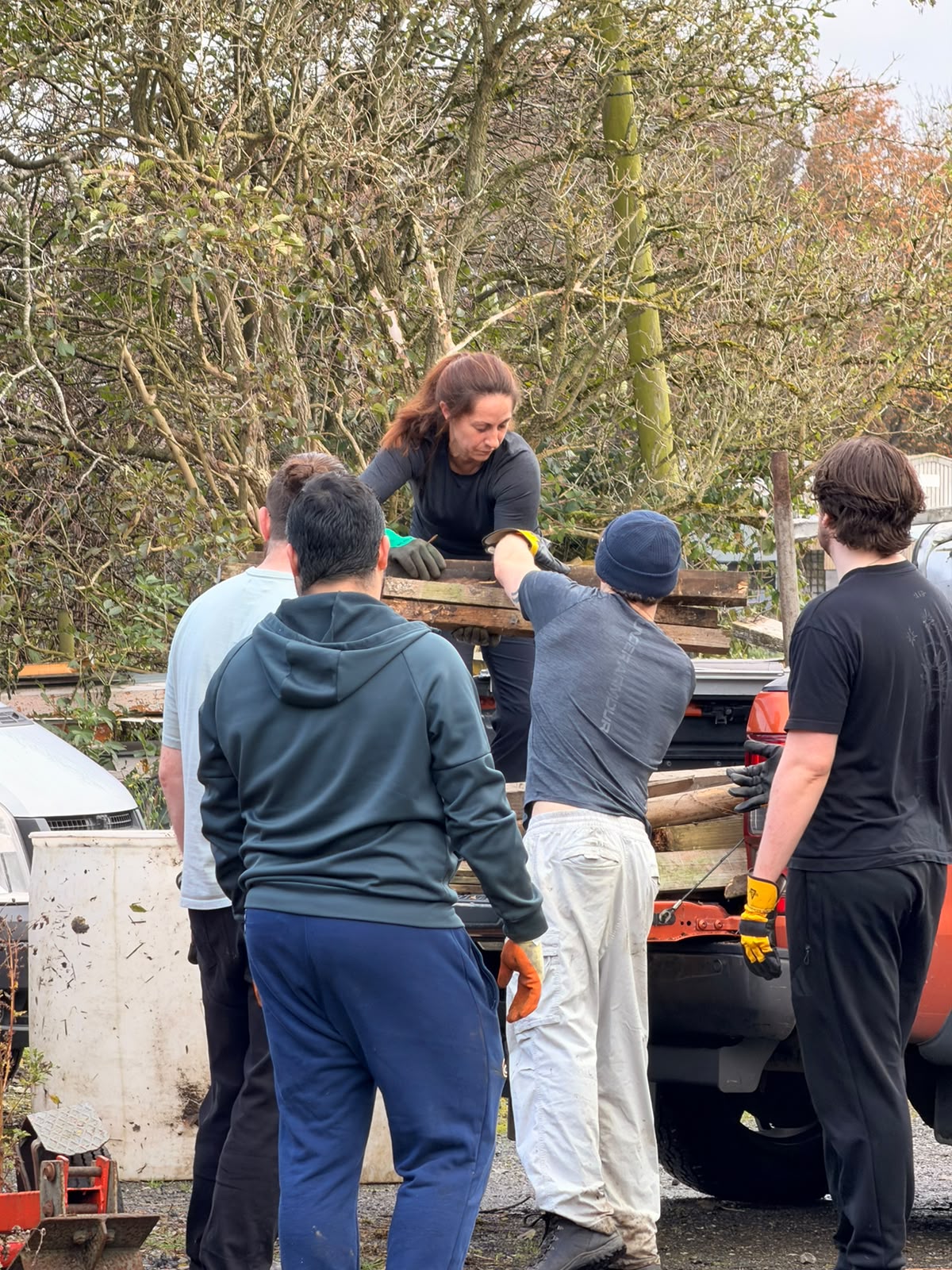 A volunteer on the back of the pickup passing planks down into the skip